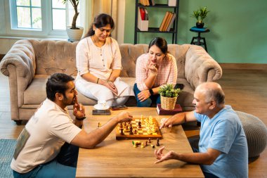 Evde kanepede satranç oynarken, dört çocuklu Hintli aile, yaşlı ebeveynler ve genç yetişkin çocuklar dahil modern konforlu oturma odasında kaliteli zaman geçirmenin keyfini çıkarıyorlar, akıllı masa oyunlarıyla kaynaşıyorlar.