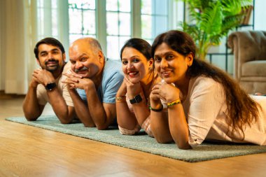 Ellerinin üzerinde yerde uzanmış, kameraya gülümsüyor, yetişkin bir oğlu ve kızı olan Hintli ebeveynler sıcak ev içlerinde birlikte poz veriyor, samimiyet, yakınlık ve birliktelik gösteriyorlar.