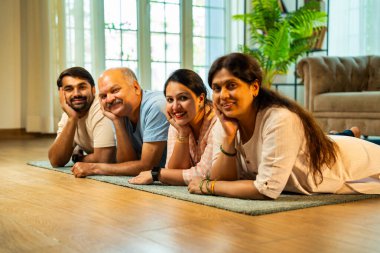Ellerinin üzerinde yerde uzanmış, kameraya gülümsüyor, yetişkin bir oğlu ve kızı olan Hintli ebeveynler sıcak ev içlerinde birlikte poz veriyor, samimiyet, yakınlık ve birliktelik gösteriyorlar.