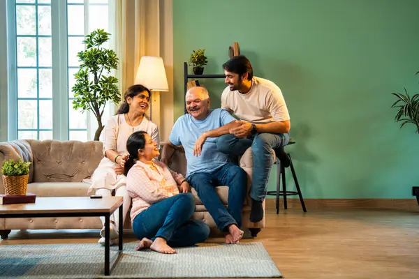 Evde otururken birlikte gülerdik. Yaşlı ebeveynleri ve küçük yetişkin çocukları olan mutlu Hintli aile modern rahat bir oturma odasında eğlenceli sohbetler yapar, kaliteli zaman geçirirdik.