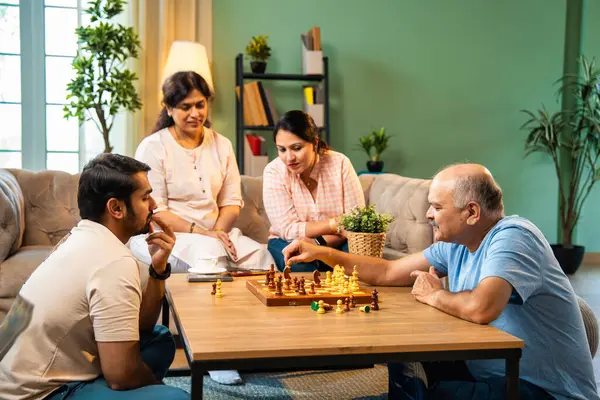 Evde kanepede satranç oynarken, dört çocuklu Hintli aile, yaşlı ebeveynler ve genç yetişkin çocuklar dahil modern konforlu oturma odasında kaliteli zaman geçirmenin keyfini çıkarıyorlar, akıllı masa oyunlarıyla kaynaşıyorlar.