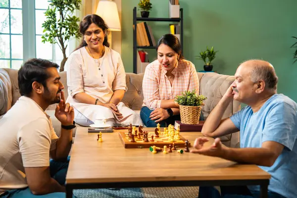 Evde kanepede satranç oynarken, dört çocuklu Hintli aile, yaşlı ebeveynler ve genç yetişkin çocuklar dahil modern konforlu oturma odasında kaliteli zaman geçirmenin keyfini çıkarıyorlar, akıllı masa oyunlarıyla kaynaşıyorlar.