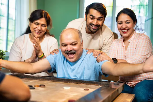 Birlikte carom ya da carrom masa üstü oyunu oynayarak, dört kişilik Hintli aile, yaşlı ebeveynler ve genç yetişkin bir çocuk ve kız evdeki boş zamanlarında rahat oturma odasında eğleniyorlar.