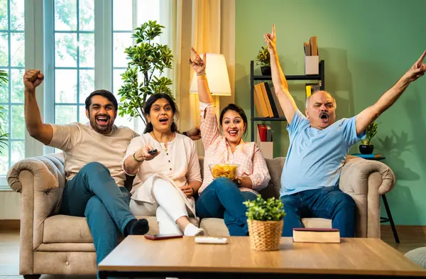 Birlikte televizyon seyretmek, dört çocuklu Hintli aile, yaşlı ebeveynler, genç yetişkin kız ve erkek çocuk modern oturma odasındaki rahat koltukta oturmuş spor ya da film izlerken tezahürat yapıyorlar.