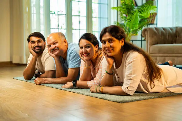 Ellerinin üzerinde yerde uzanmış, kameraya gülümsüyor, yetişkin bir oğlu ve kızı olan Hintli ebeveynler sıcak ev içlerinde birlikte poz veriyor, samimiyet, yakınlık ve birliktelik gösteriyorlar.