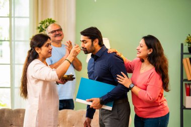 Genç Hintli bir adam iş görüşmesini kırar, üst düzey ebeveynler ve kız kardeşlerle tanışmak için yönetici kıyafetiyle eve döner, aileye sarılır, kutsanmak ister, başarıyı kutlar ve neşeli duygusal anı paylaşır.