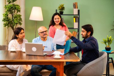 Hintli kıdemli bir adam, genç yönetici olarak belgeyi imzalarken ona yol gösteriyor. Rahat modern bir evde eşi ve kızının yanında oturuyor. Vasiyeti, yasal belgeleri, finans veya sigorta danışmanlığını sembolize ediyor.