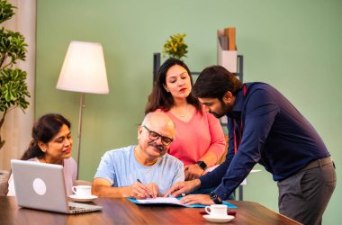 Hintli kıdemli bir adam, genç yönetici olarak belgeyi imzalarken ona yol gösteriyor. Rahat modern bir evde eşi ve kızının yanında oturuyor. Vasiyeti, yasal belgeleri, finans veya sigorta danışmanlığını sembolize ediyor.