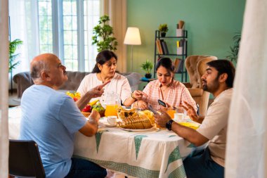 Birlikte kahvaltı ederken, Hintli üst düzey ebeveynler ve genç yetişkin kız ve erkek çocuk yemek masasında rahat, modern bir evde oturmuş yemek saatinde akıllı telefon kullanımı ve dijital dikkat dağınıklığı üzerine tartışıyorlardı.