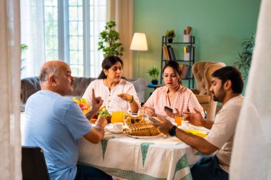 Birlikte kahvaltı ederken, Hintli üst düzey ebeveynler ve genç yetişkin kız ve erkek çocuk yemek masasında rahat, modern bir evde oturmuş yemek saatinde akıllı telefon kullanımı ve dijital dikkat dağınıklığı üzerine tartışıyorlardı.