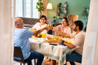 Neşeli tostlar içinde samosa yetiştirmek, mutlu Hintli aile üst düzey ebeveynler ve genç yetişkin kız ve erkek çocuklar sabahları modern sıcak ev yemeği masasında keyifli bir kahvaltı yapıyorlar.