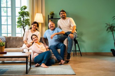 Evde otururken birlikte gülerdik. Yaşlı ebeveynleri ve küçük yetişkin çocukları olan mutlu Hintli aile modern rahat bir oturma odasında eğlenceli sohbetler yapar, kaliteli zaman geçirirdik.