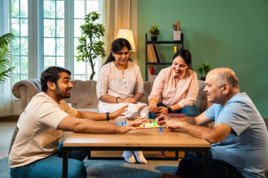 Kapalı alanlarda ludo masası oyunu oynuyorlar, dört kişilik Hint ailesi, yaşlı ebeveynler, genç yetişkin bir çocuk ve kız evdeki modern sıcak oturma odasında birlikte otururken kaliteli vakit geçirmenin keyfini çıkarıyorlar.