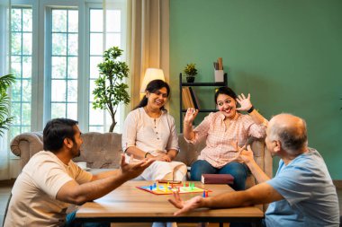 Kapalı alanlarda ludo masası oyunu oynuyorlar, dört kişilik Hint ailesi, yaşlı ebeveynler, genç yetişkin bir çocuk ve kız evdeki modern sıcak oturma odasında birlikte otururken kaliteli vakit geçirmenin keyfini çıkarıyorlar.