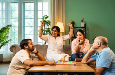 Kapalı alanlarda ludo masası oyunu oynuyorlar, dört kişilik Hint ailesi, yaşlı ebeveynler, genç yetişkin bir çocuk ve kız evdeki modern sıcak oturma odasında birlikte otururken kaliteli vakit geçirmenin keyfini çıkarıyorlar.