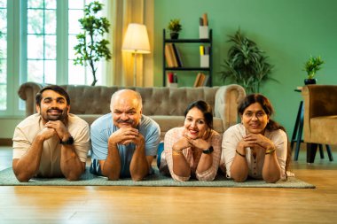 Ellerinin üzerinde yerde uzanmış, kameraya gülümsüyor, yetişkin bir oğlu ve kızı olan Hintli ebeveynler sıcak ev içlerinde birlikte poz veriyor, samimiyet, yakınlık ve birliktelik gösteriyorlar.