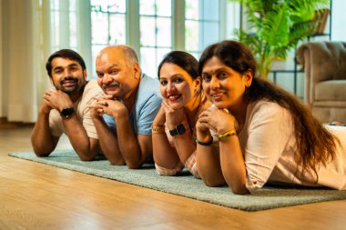 Ellerinin üzerinde yerde uzanmış, kameraya gülümsüyor, yetişkin bir oğlu ve kızı olan Hintli ebeveynler sıcak ev içlerinde birlikte poz veriyor, samimiyet, yakınlık ve birliktelik gösteriyorlar.