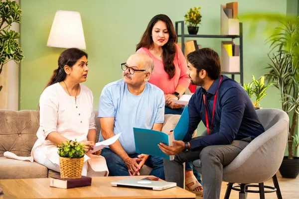 Genç kızı olan Hintli üst düzey bir çift, emlak kredisi veya tasarruf danışmanlığı kavramında resmi giyimde erkek danışman veya banka temsilcisiyle mali evrakları tartışıyor.