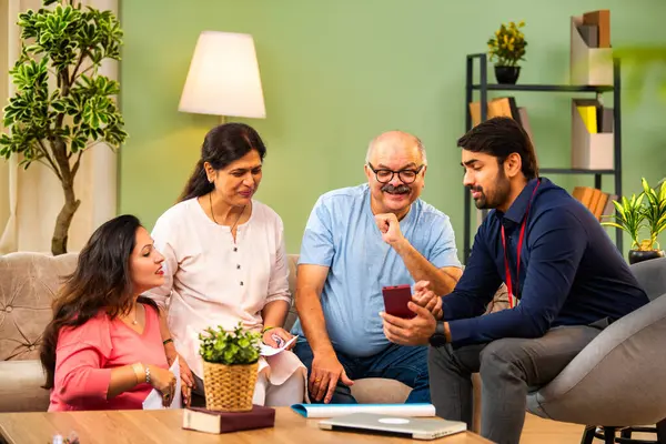 Genç kızı olan Hintli yaşlı bir çift evde akıllı telefondan detayları gösteren erkek danışmanla mali belgeleri tartışıyor. Sigorta, gayrimenkul, tasarruf, kredi, yatırım toplantısı
