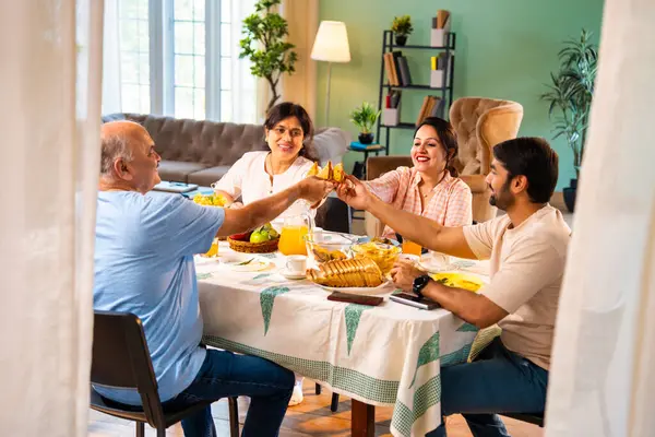Neşeli tostlar içinde samosa yetiştirmek, mutlu Hintli aile üst düzey ebeveynler ve genç yetişkin kız ve erkek çocuklar sabahları modern sıcak ev yemeği masasında keyifli bir kahvaltı yapıyorlar.