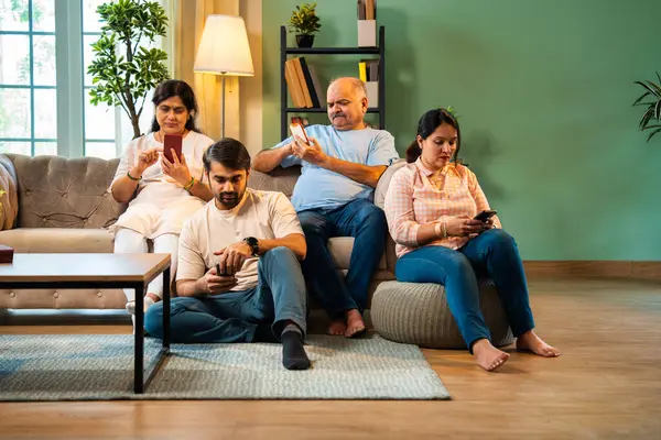 Akıllı telefonlar kullanarak kanepede oturmak, Hintli ailelerin aileleri modern rahat oturma odalarında küçük çocuklar, hepsi mobil ekran bağımlısı bir aile olarak etkileşim ya da bağ kurma zamanı olmadan