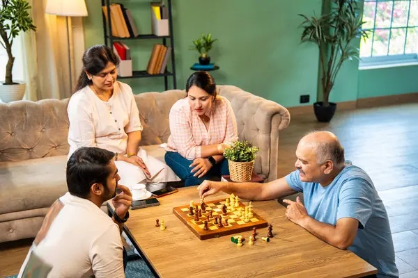 Evde kanepede satranç oynarken, dört çocuklu Hintli aile, yaşlı ebeveynler ve genç yetişkin çocuklar dahil modern konforlu oturma odasında kaliteli zaman geçirmenin keyfini çıkarıyorlar, akıllı masa oyunlarıyla kaynaşıyorlar.