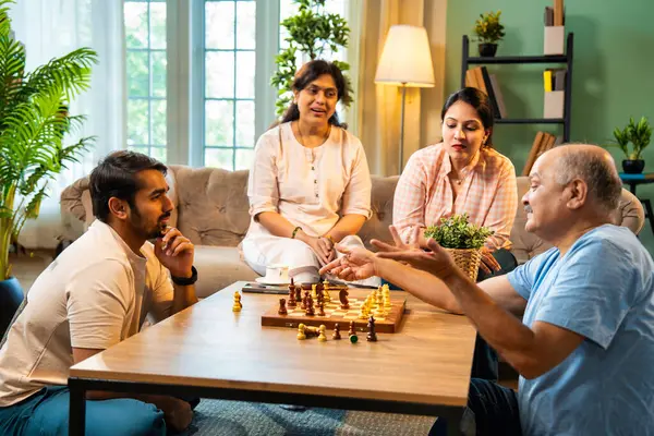 Evde kanepede satranç oynarken, dört çocuklu Hintli aile, yaşlı ebeveynler ve genç yetişkin çocuklar dahil modern konforlu oturma odasında kaliteli zaman geçirmenin keyfini çıkarıyorlar, akıllı masa oyunlarıyla kaynaşıyorlar.