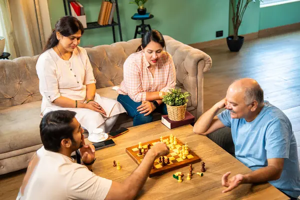 Evde kanepede satranç oynarken, dört çocuklu Hintli aile, yaşlı ebeveynler ve genç yetişkin çocuklar dahil modern konforlu oturma odasında kaliteli zaman geçirmenin keyfini çıkarıyorlar, akıllı masa oyunlarıyla kaynaşıyorlar.