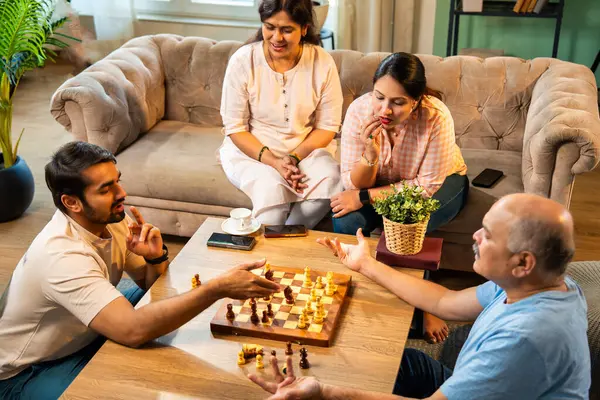 Evde kanepede satranç oynarken, dört çocuklu Hintli aile, yaşlı ebeveynler ve genç yetişkin çocuklar dahil modern konforlu oturma odasında kaliteli zaman geçirmenin keyfini çıkarıyorlar, akıllı masa oyunlarıyla kaynaşıyorlar.