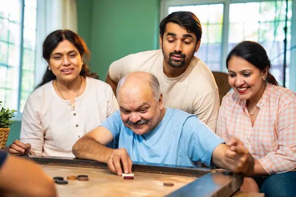 Birlikte carom ya da carrom masa üstü oyunu oynayarak, dört kişilik Hintli aile, yaşlı ebeveynler ve genç yetişkin bir çocuk ve kız evdeki boş zamanlarında rahat oturma odasında eğleniyorlar.