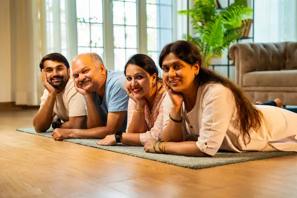 Ellerinin üzerinde yerde uzanmış, kameraya gülümsüyor, yetişkin bir oğlu ve kızı olan Hintli ebeveynler sıcak ev içlerinde birlikte poz veriyor, samimiyet, yakınlık ve birliktelik gösteriyorlar.