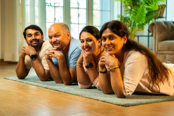 Ellerinin üzerinde yerde uzanmış, kameraya gülümsüyor, yetişkin bir oğlu ve kızı olan Hintli ebeveynler sıcak ev içlerinde birlikte poz veriyor, samimiyet, yakınlık ve birliktelik gösteriyorlar.