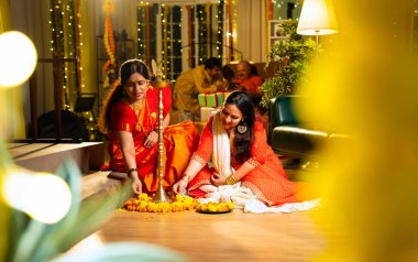 Samai 'nin etrafındaki çiçek Rangoli' sini süsleyen Hintli genç kız geleneksel Hindu kıdemli anne Hint festivali için neşe içinde hazırlanıyor Diwali akşam saatlerinde kapalı bir yerde moda ve renkli tasarım ile kutlama yapıyor.
