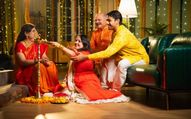 Diwali 'de evde samai diya aydınlatması, Hintli dört kişilik Hint ailesi sari, baba, genç kız ve koca Hindu festivalini neşe ve gelenekle kutlarken birlikte gülümsüyor.
