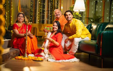 Diwali 'de evde samai diya aydınlatması, Hintli dört kişilik Hint ailesi sari, baba, genç kız ve koca Hindu festivalini neşe ve gelenekle kutlarken birlikte gülümsüyor.