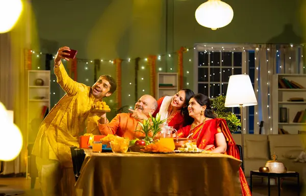 Yemek masasında selfie çeken dört kişilik Hintli aile, kıdemli ebeveynleri, yetişkin oğulları ve kızları ile Diwali festivalini içeride dekorasyonlar, tatlılar ve gülücüklerle kutluyor.