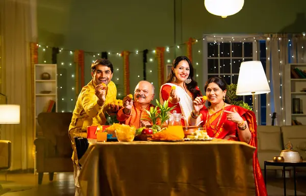 Laddu 'yu kameraya gösteriyoruz, Hintli dört çocuklu Hintli aile. Hindu festivalini kutlayan yetişkin bir aile. Diwali içeride, dekore edilmiş yemek masasında, gülümsüyor ve birlikte eğleniyorlar.
