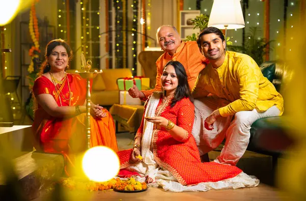 Diwali 'de evde samai diya aydınlatması, Hintli dört kişilik Hint ailesi sari, baba, genç kız ve koca Hindu festivalini neşe ve gelenekle kutlarken birlikte gülümsüyor.