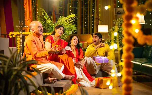 Ladus 'u kucaklayan ve birlikte gülümseyen Hintli aile, genç bir kızla birlikte, sari giymiş yaşlı bir anne, geleneksel giysili baba ve koca Diwali' yi kapalı mekanda kutluyor, çiçek rangoli ve kahkahalarla.