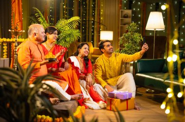 Latdu 'yla Diwali selfie, genç kızla Hintli aile, sari giyen yaşlı anne, geleneksel giyimli baba ve koca Hindu festivalini dekore edilmiş evde diya rangoli ile kutluyorlar.