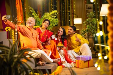 Latdu 'yla Diwali selfie, genç kızla Hintli aile, sari giyen yaşlı anne, geleneksel giyimli baba ve koca Hindu festivalini dekore edilmiş evde diya rangoli ile kutluyorlar.