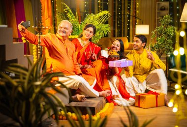 Latdu 'yla Diwali selfie, genç kızla Hintli aile, sari giyen yaşlı anne, geleneksel giyimli baba ve koca Hindu festivalini dekore edilmiş evde diya rangoli ile kutluyorlar.