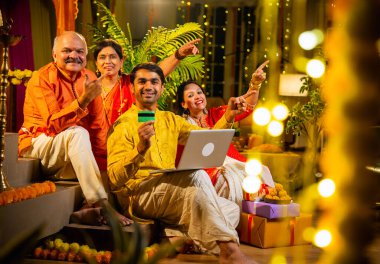 İnternetten bilgisayar ve kredi kartı kullanarak alışveriş yapan, karısı olan Hintli genç adam, geleneksel kıdemli ebeveynler evde Diwali gecesini kutluyorlar, para, çiçek ve ev dekorasyonlarıyla birlikte oturuyorlar.