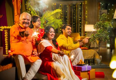 Diwali gecesinde ışıltıların tadını çıkaran Hintli aile, genç bir kızla, sari giymiş yaşlı bir anne, geleneksel elbiseli baba ve koca diya, çiçek rangoli, havai fişek sevinci ile şenlik basamaklarında oturuyor.