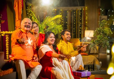 Diwali gecesinde ışıltıların tadını çıkaran Hintli aile, genç bir kızla, sari giymiş yaşlı bir anne, geleneksel elbiseli baba ve koca diya, çiçek rangoli, havai fişek sevinci ile şenlik basamaklarında oturuyor.