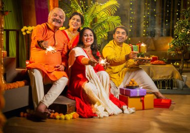 Diwali gecesinde ışıltıların tadını çıkaran Hintli aile, genç bir kızla, sari giymiş yaşlı bir anne, geleneksel elbiseli baba ve koca diya, çiçek rangoli, havai fişek sevinci ile şenlik basamaklarında oturuyor.
