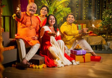 Diwali gecesinde ışıltıların tadını çıkaran Hintli aile, genç bir kızla, sari giymiş yaşlı bir anne, geleneksel elbiseli baba ve koca diya, çiçek rangoli, havai fişek sevinci ile şenlik basamaklarında oturuyor.