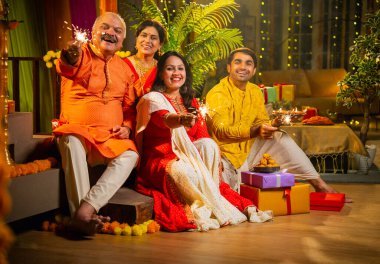Diwali gecesinde ışıltıların tadını çıkaran Hintli aile, genç bir kızla, sari giymiş yaşlı bir anne, geleneksel elbiseli baba ve koca diya, çiçek rangoli, havai fişek sevinci ile şenlik basamaklarında oturuyor.