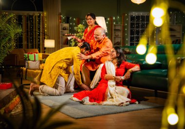 Oğul, anne ve babasından Diwali duası almak için şenlikli bir evde anne, baba ve genç kız oğulla sıcak bir jestle selamlaştıktan sonra televizyonda komik bir program izliyorlar.