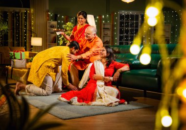 Oğul, anne ve babasından Diwali duası almak için şenlikli bir evde anne, baba ve genç kız oğulla sıcak bir jestle selamlaştıktan sonra televizyonda komik bir program izliyorlar.